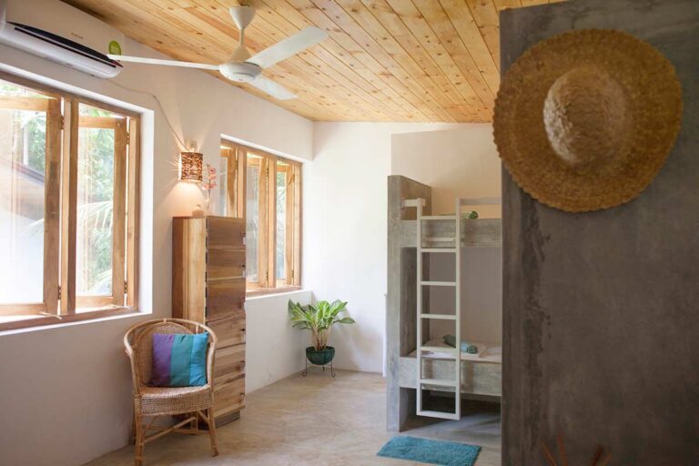 Dormitory room with wooden bunk beds and rattan armchair at Salt House, Hiriketiya Bay, Sri Lanka