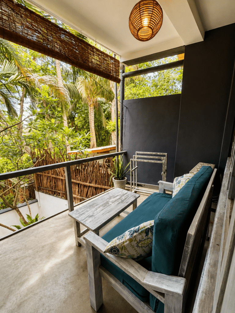 Private balcony with a cushioned bench, small table and pendant lamp overlooking tropical trees at Salt House, Hiriketiya Bay, Sri Lanka
