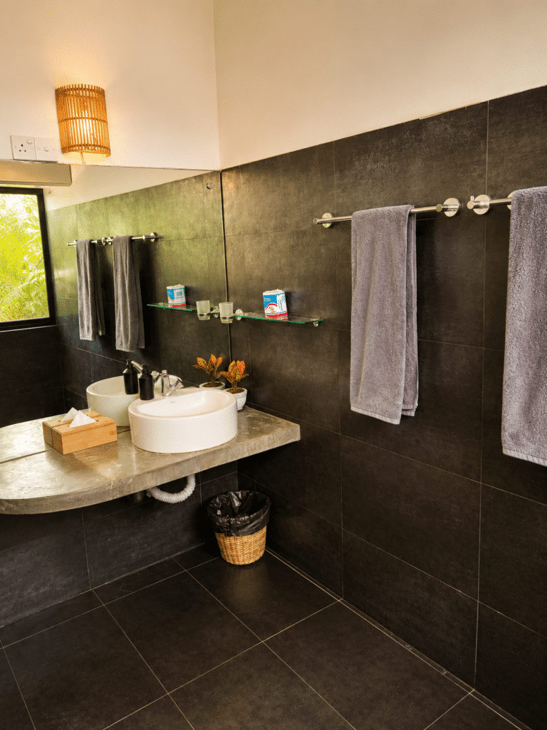 Bathroom with dark grey tiling, a vessel sink, large mirror and hanging towels at Salt House, Hiriketiya Bay, Sri Lanka