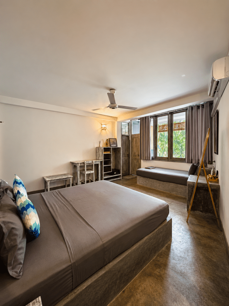Bedroom with a dark brown bedspread, wood flooring, ceiling fan and a window bench seat at Salt House, Hiriketiya Bay, Sri Lanka